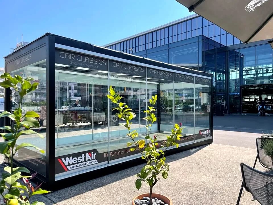 REINHART Gallery Car Classics frontal bei Tageslicht, Glasfront geöffnet, Sportwagen im Inneren sichtbar. Projektfoto.